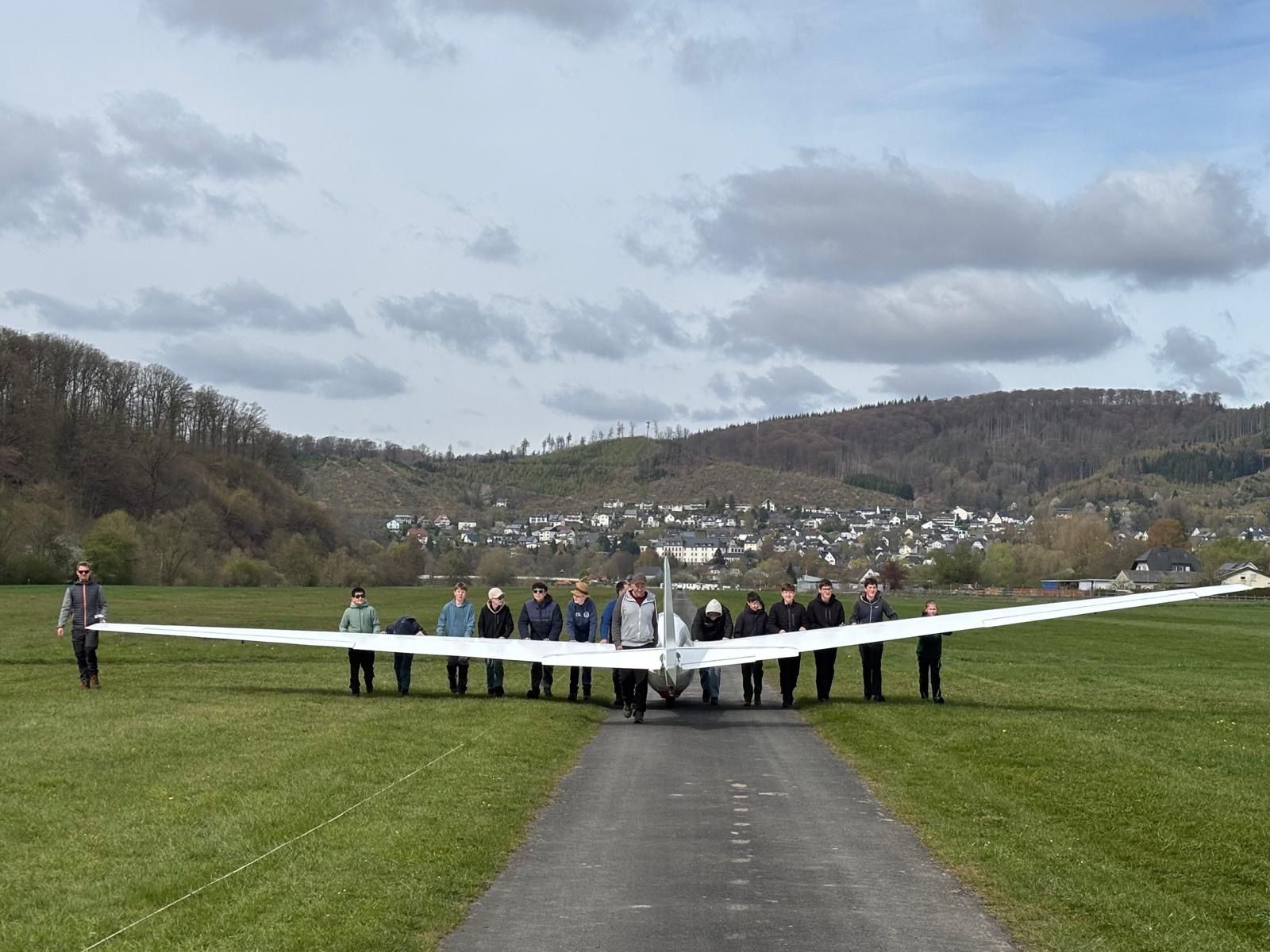 Jugendgruppe schiebt gemeinsam ein Segelflugzeug über die Piste