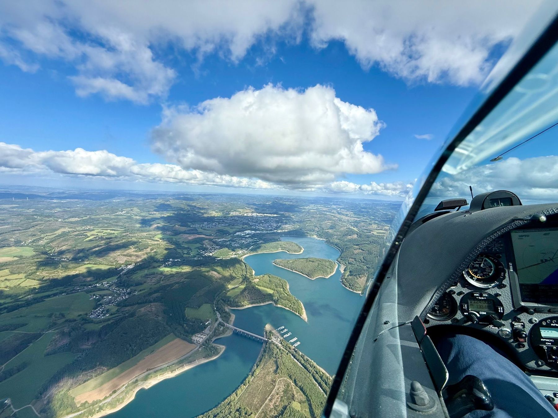 Blick aus dem Cockpit über einen Stausee im Sauerland unter Cumuluswolken